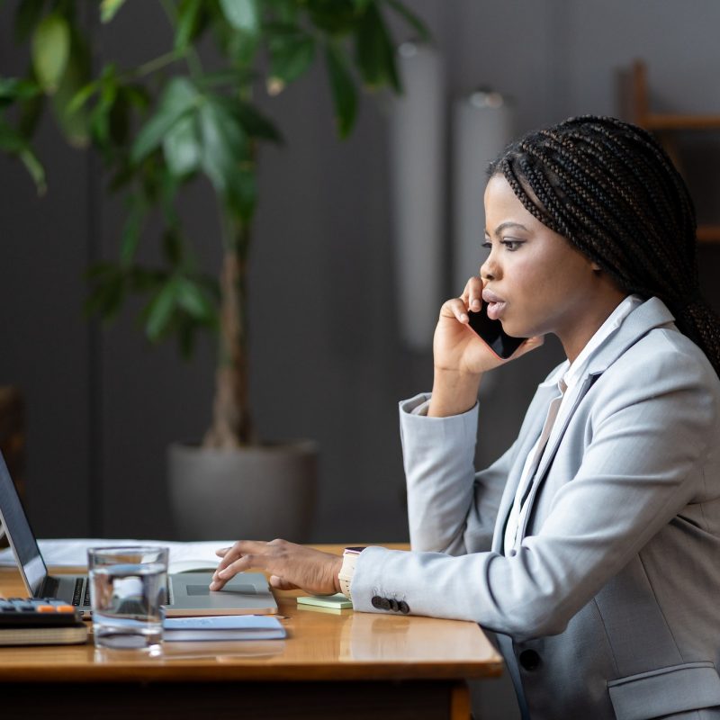 afro-female-business-consultant-interacting-with-client-over-phone-and-entering-data-on-laptop.jpg